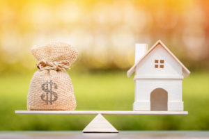 a money bag and a house on a balancing scale.