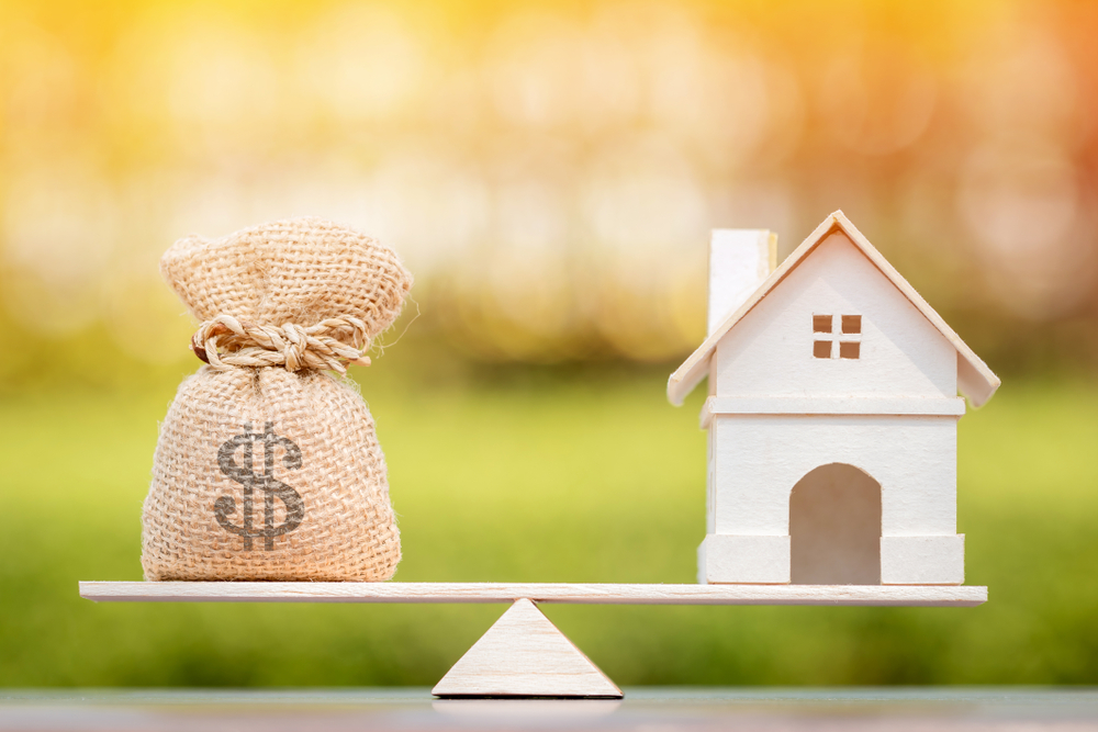 a money bag and a house on a balancing scale.