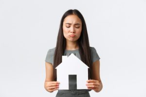 woman holding a paper house with sad face - house wont sell concept.